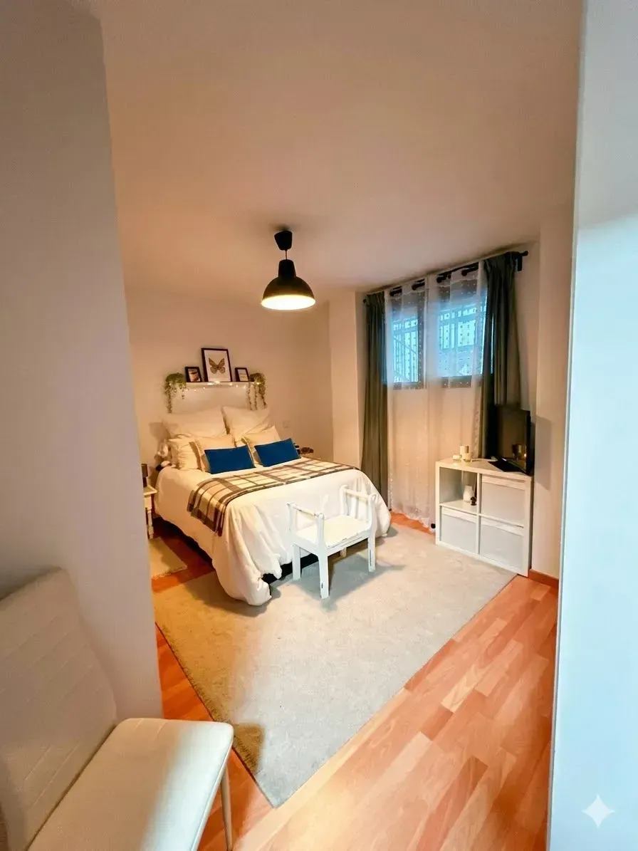 Acogedora habitación con cama blanca, detalles en azul, ventana, cortinas y suelo de madera.