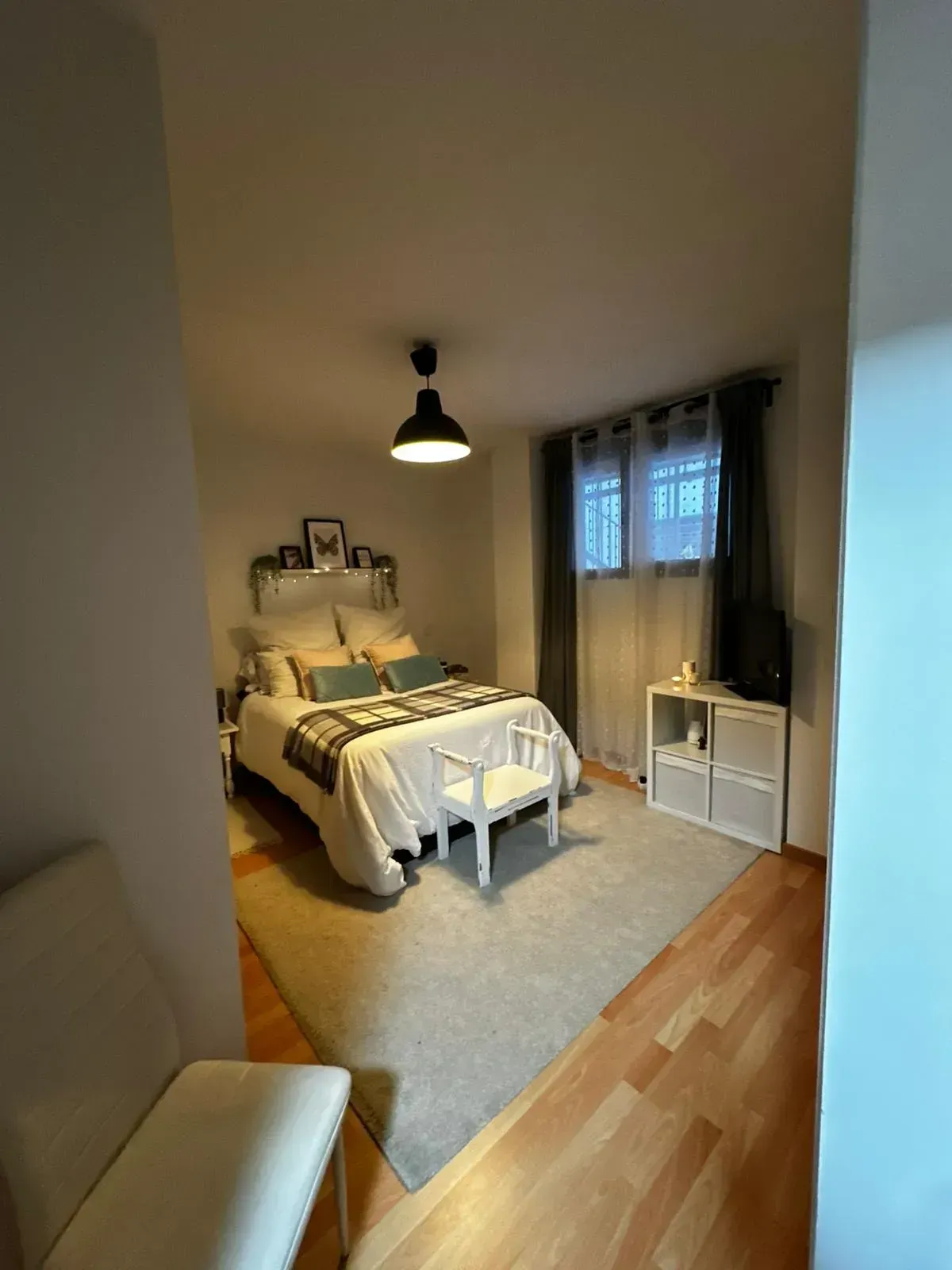 Habitación acogedora con cama blanca, alfombra gris, cortinas y lámparas colgantes cálidas.