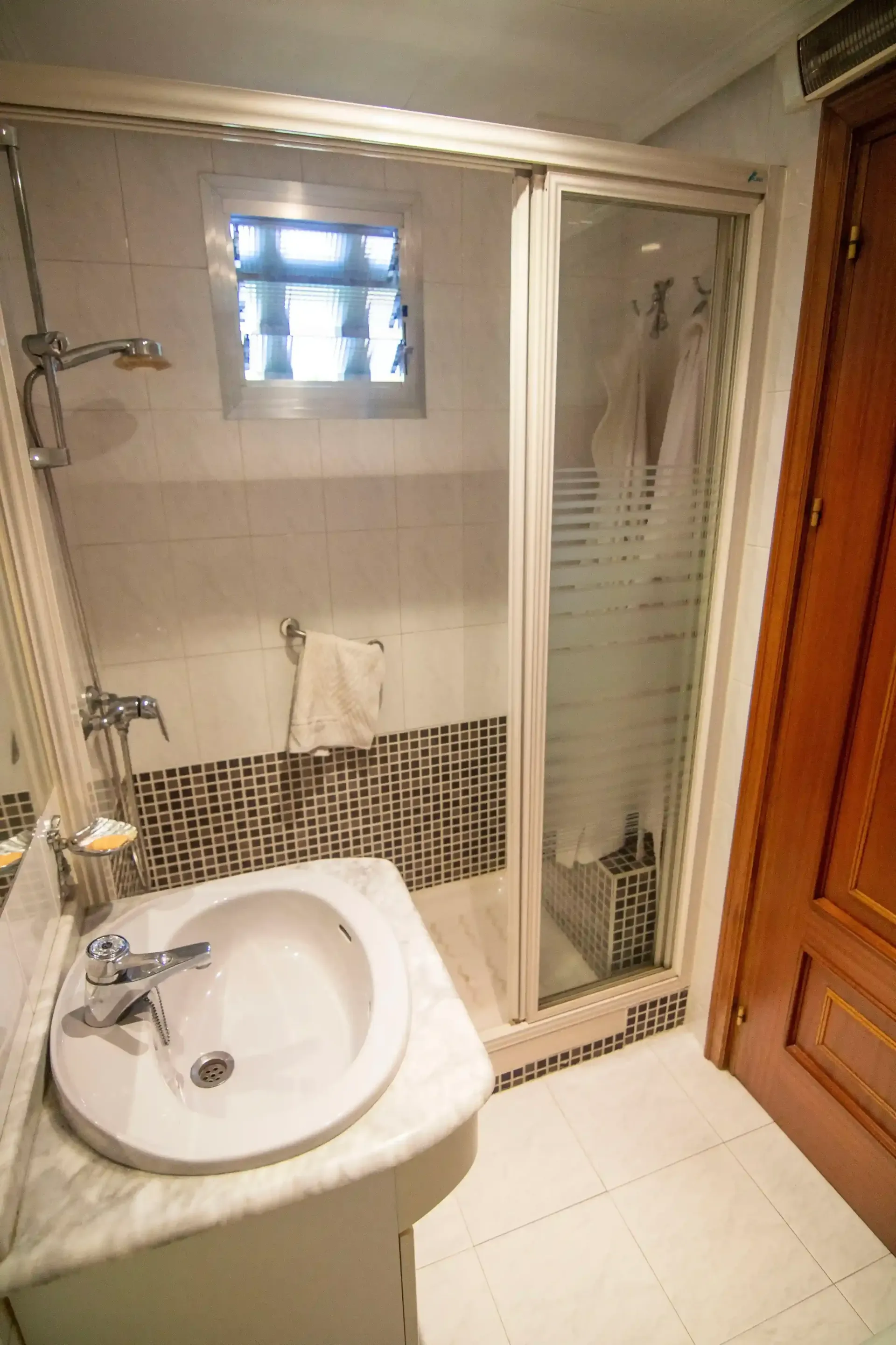 Baño pequeño con lavabo, inodoro, cabina de ducha esmerilada y suelo de baldosas.