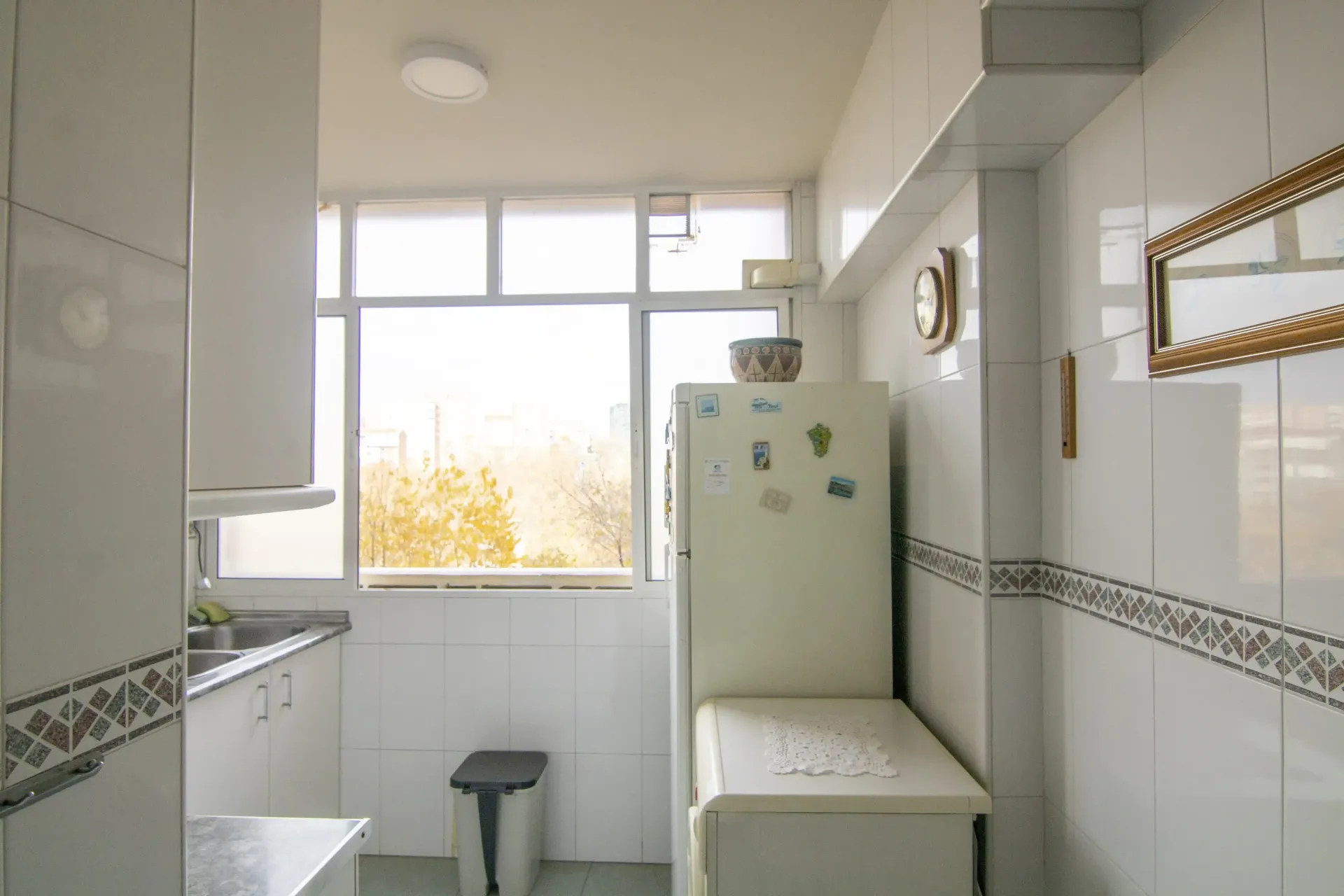 Baño blanco luminoso con ventana, lavabo, inodoro y armario con espejo.