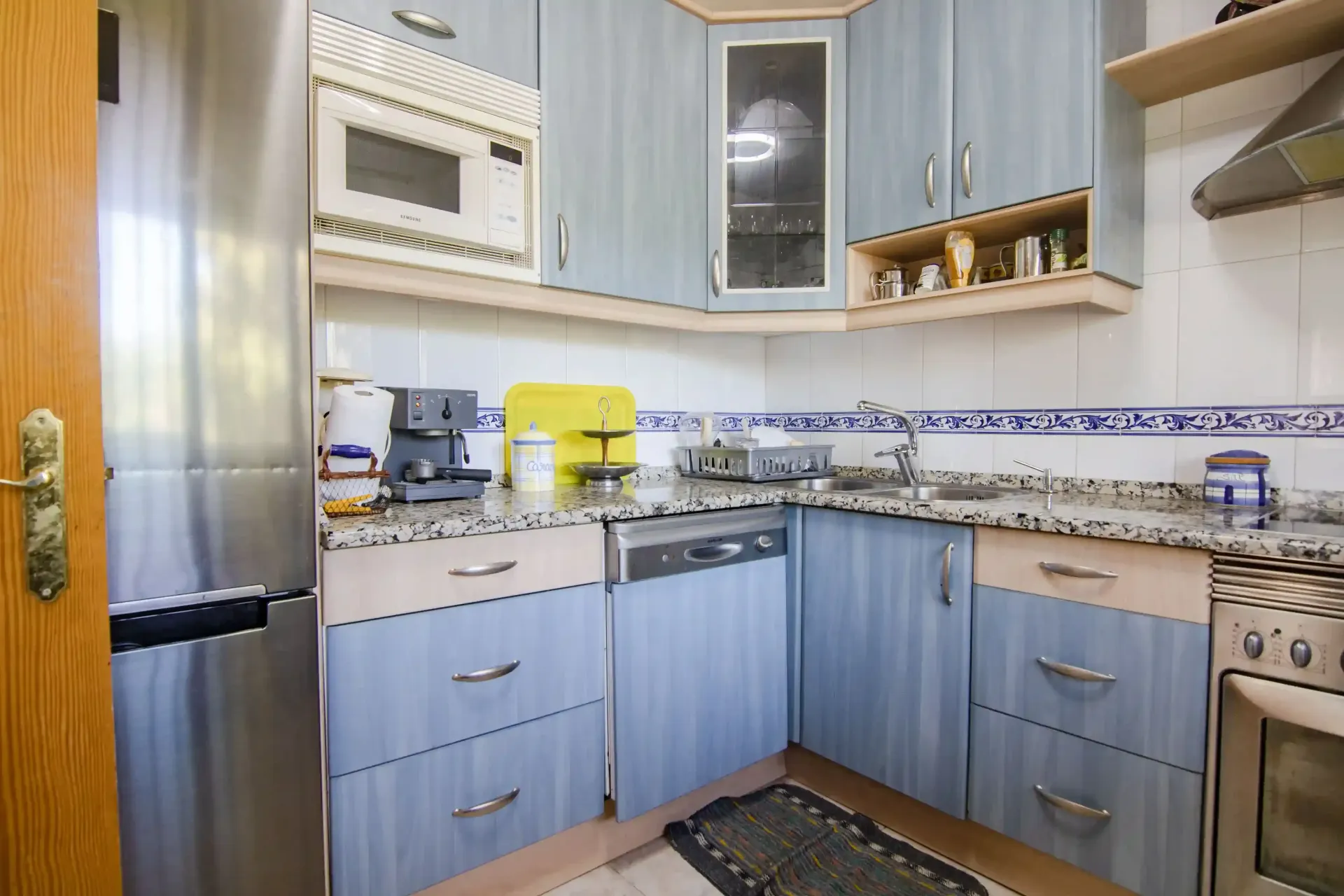 Cocina pequeña con armarios azules, salpicadero de azulejos blancos y microondas encima de la encimera.
