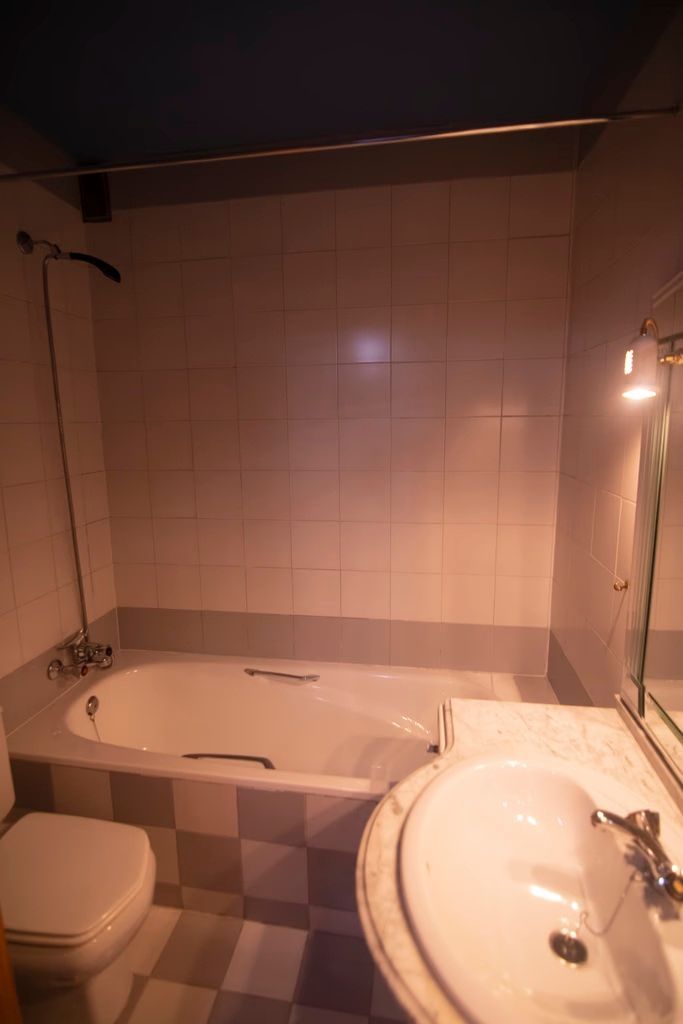 Baño pequeño con bañera, lavabo, inodoro y paredes alicatadas con iluminación cálida.