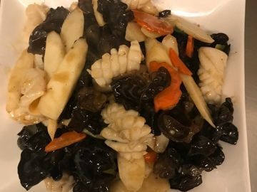 Ein weißer Teller, belegt mit verschiedenen Gemüsesorten, unter anderem Tintenfisch und Karotten.