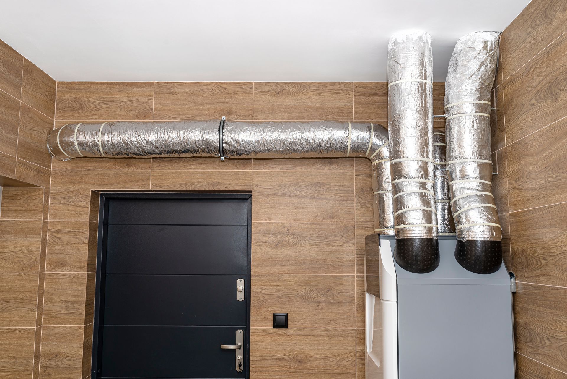 Installation de conduits d’aération en aluminium à côté de la porte noire d'un local