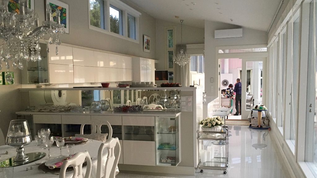 Kirkas ruokailuhuone, jossa on keittiösaareke ja katettu pöytä ateriaa varten. Valkoiset kaapit, lasivitriinit ja korkeat ikkunat.