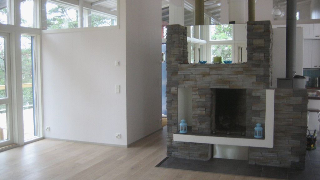 Moderni olohuone, jossa kivitakka, ikkunat ja vaaleat puulattiat.