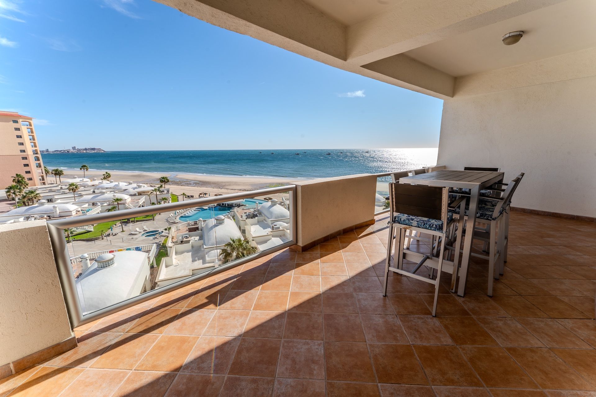 Beachfront patio with white furniture overlooking the ocean and beach on a sunny day.