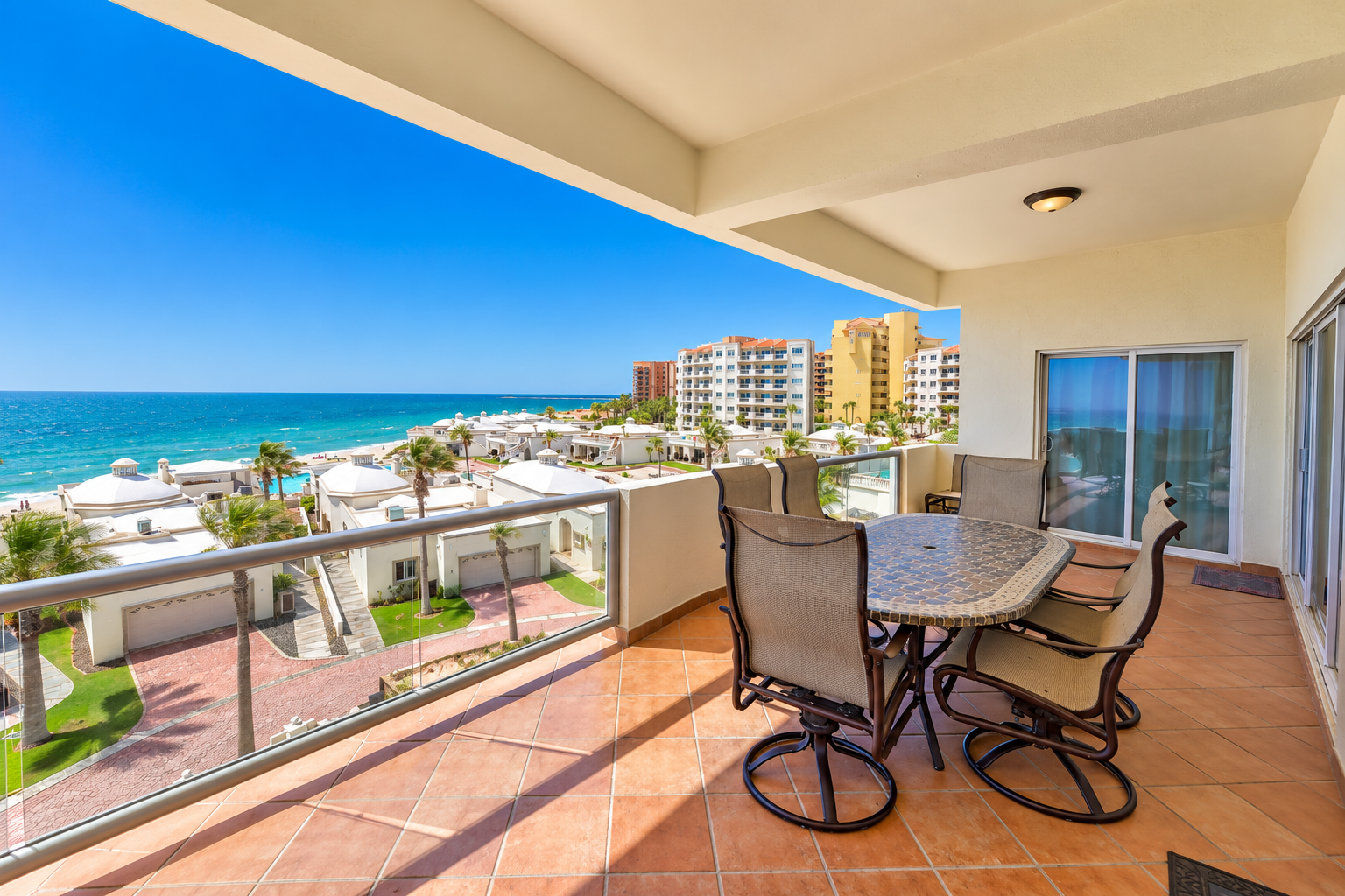 Beachfront patio with white furniture overlooking the ocean and beach on a sunny day.