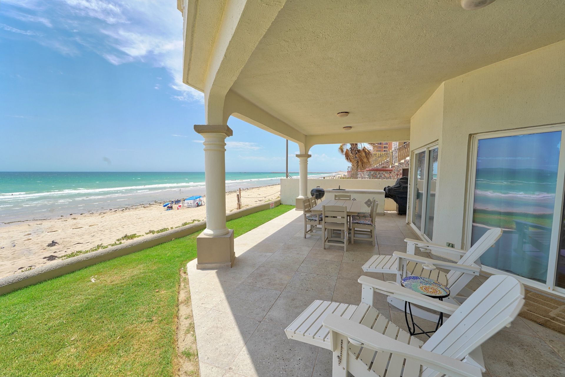 Beachfront patio with white furniture overlooking the ocean and beach on a sunny day.