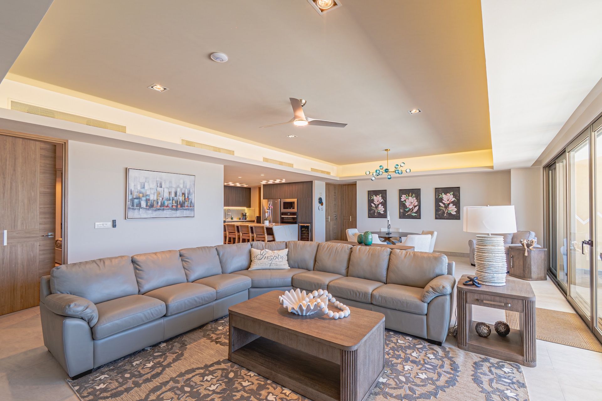 Living room with gray sectional sofa, coffee table, and rug. Open to kitchen and dining area with ocean view.