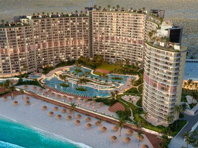 Aerial view of a curved, high-rise beach resort with an expansive pool complex and rows of umbrellas on the sand.