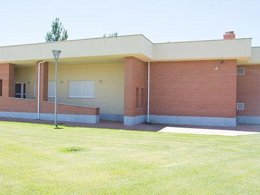 Un gran edificio de ladrillo con techo blanco está rodeado por un exuberante campo verde.