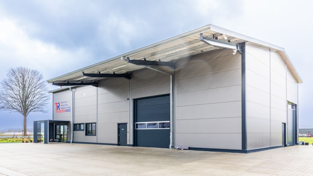 Ein großes weißes Gebäude mit einem schwarzen Garagentor und einem Baum davor.