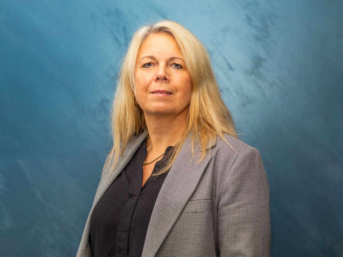 Eine Frau im Anzug steht vor einer blauen Wand.