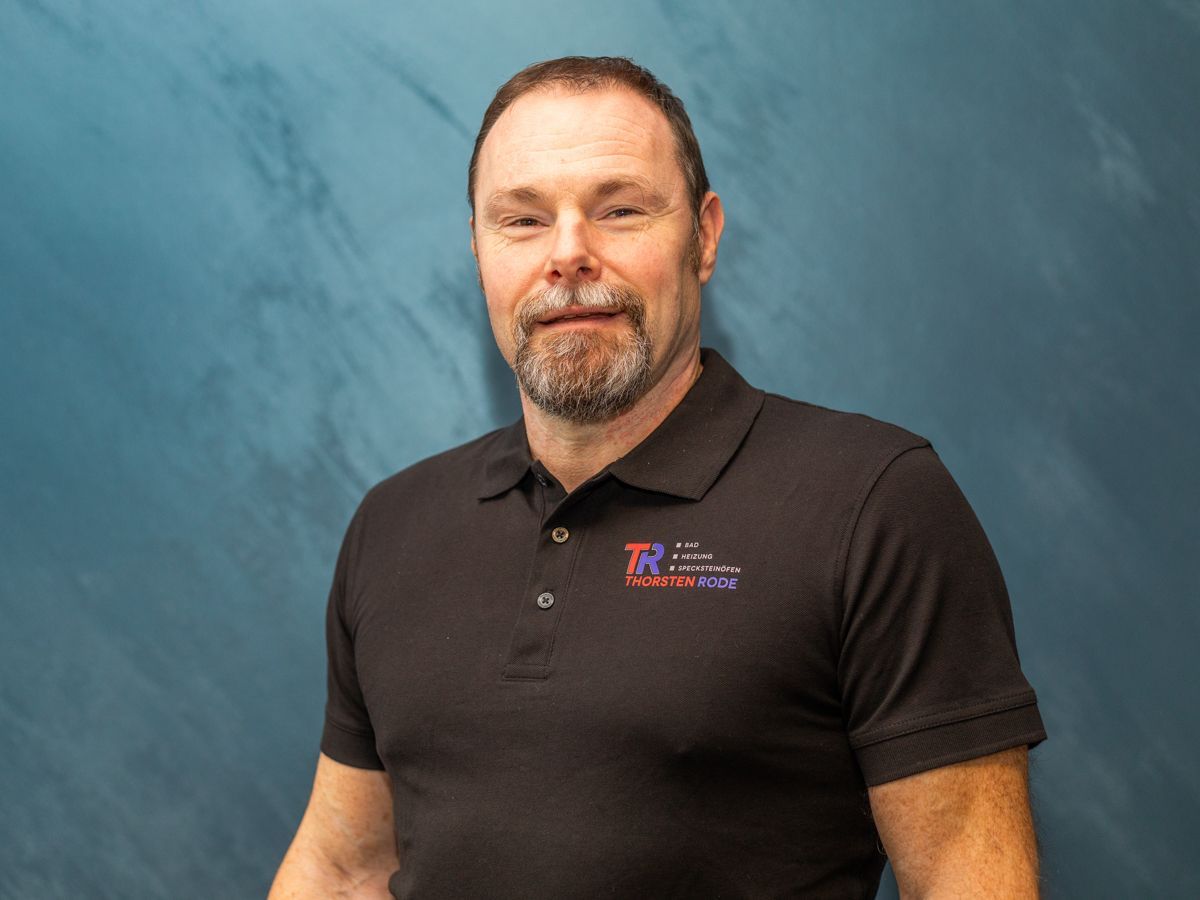 Ein Mann mit Bart trägt ein schwarzes Poloshirt.