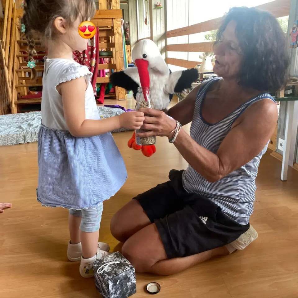 Une femme est agenouillée à côté d'une petite fille tenant une cigogne en peluche