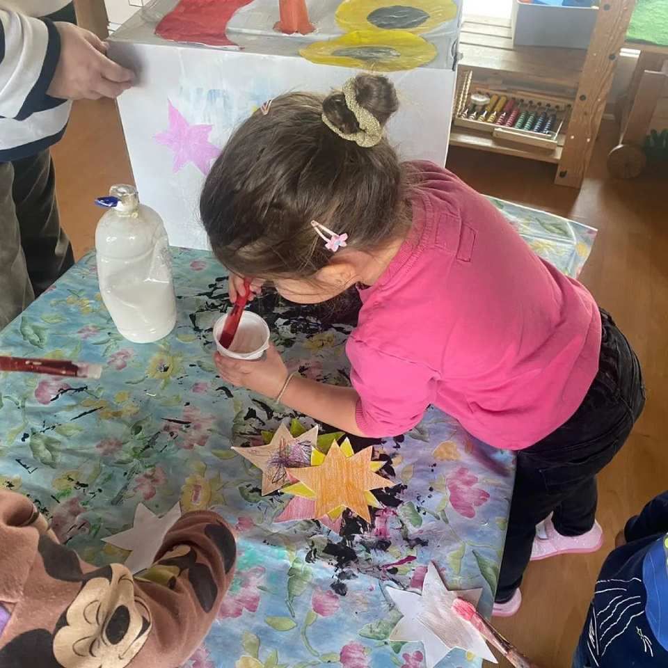 Une petite fille en chemise rose peint sur une table.