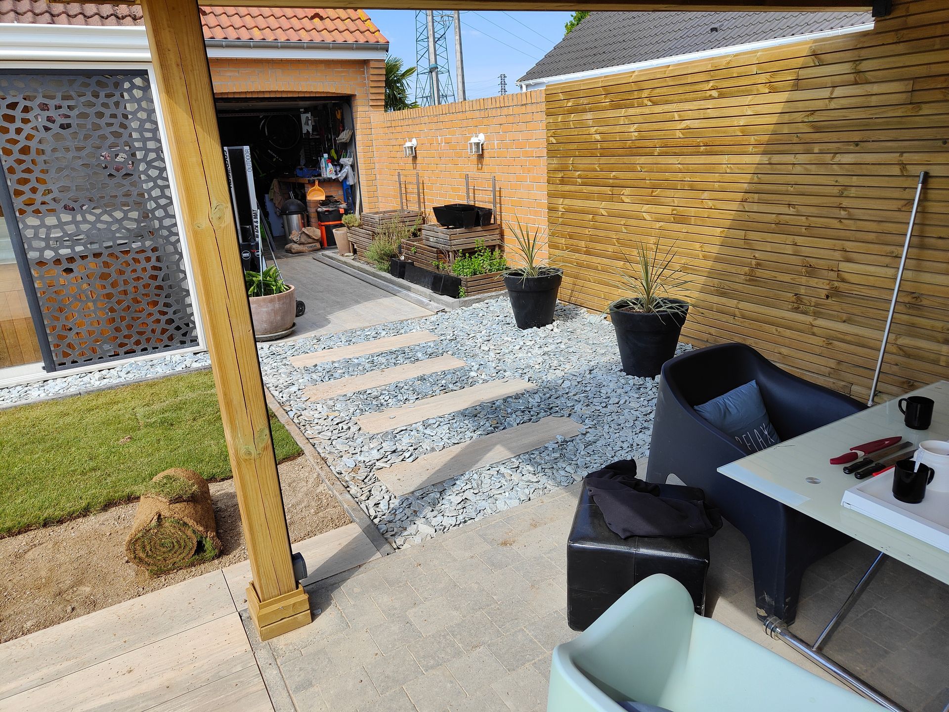 Terrasse arrière avec marches en pierre, clôture en bambou, chaises noires et petite table ensoleillée