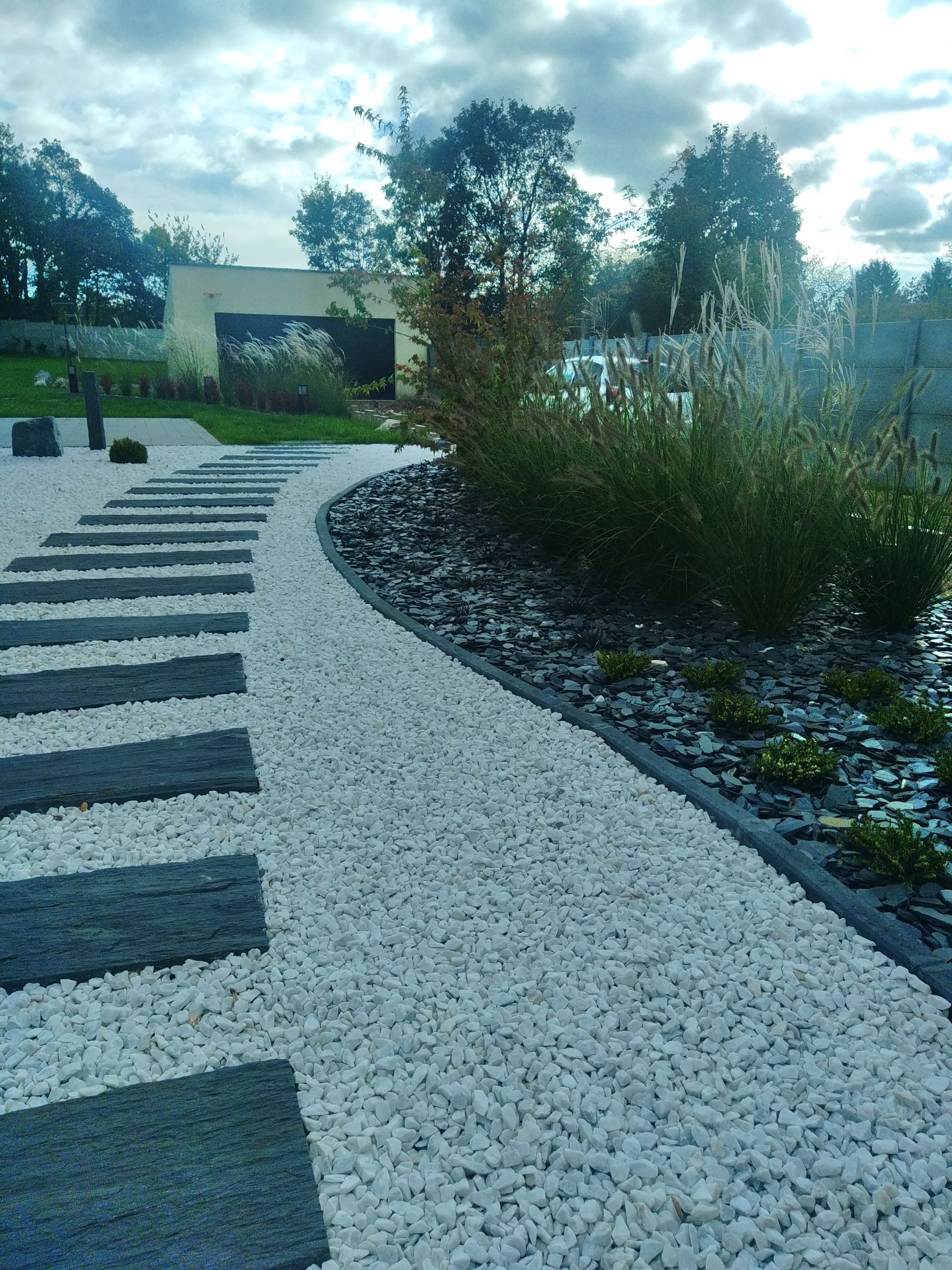 Allée de jardin sinueuse en gravier avec des dalles sombres bordant une végétation luxuriante.