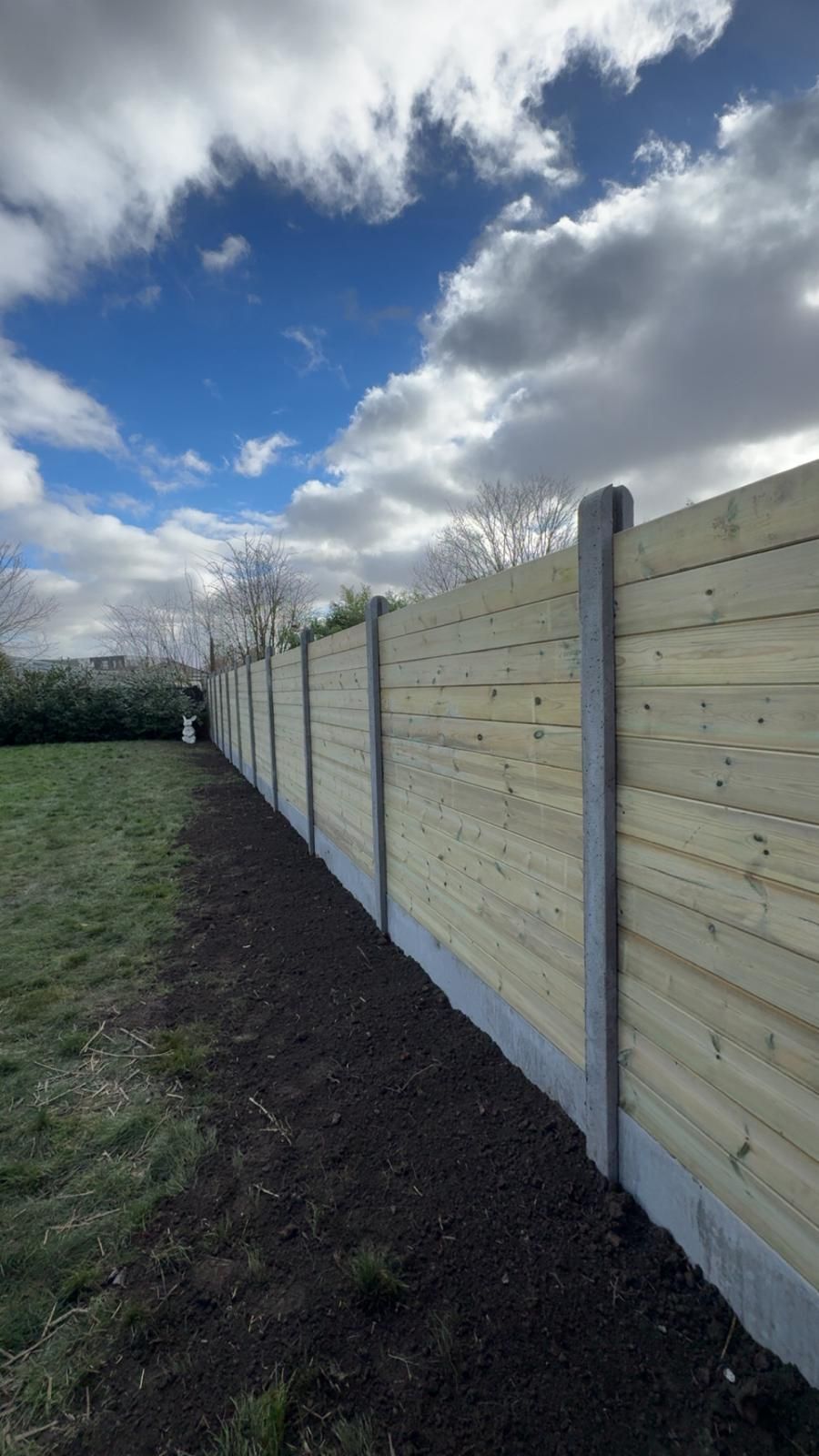 Nouvelle clôture en bois le long d'une cour herbeuse sous un ciel nuageux