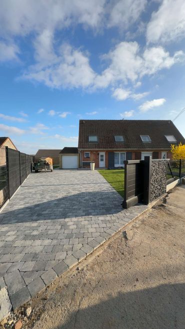 Allée pavée menant à une maison équipée de panneaux solaires sous un ciel partiellement nuageux
