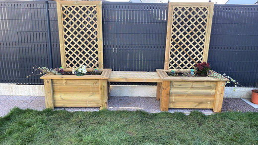 Deux jardinières en bois avec treillis sont adossées à une clôture sombre dans un jardin arrière.