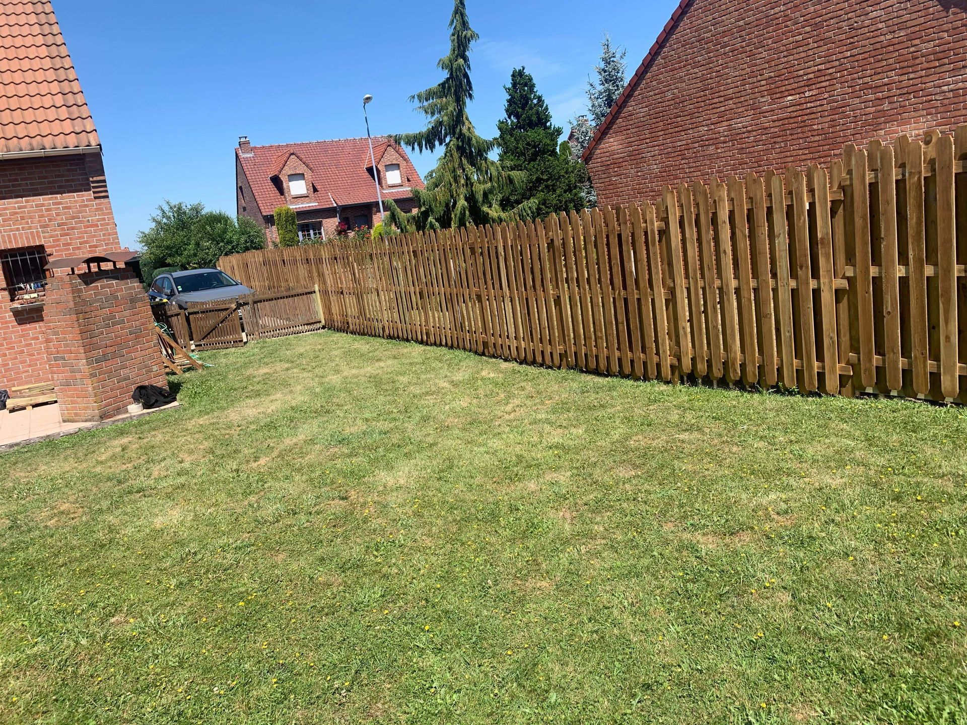 Pelouse arrière avec clôture en bois, maisons en briques et ciel bleu