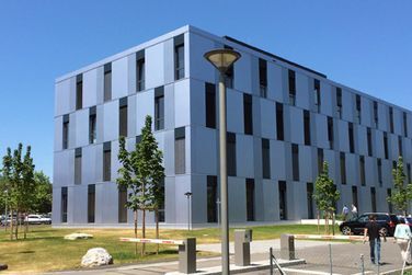 Ein großes Gebäude mit vielen Fenstern ist von Bäumen und Gras umgeben.