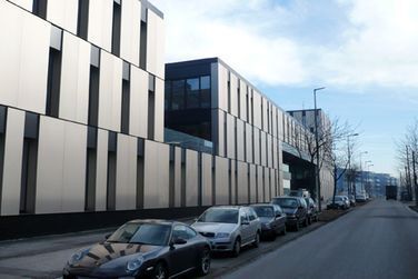 Vor einem großen Gebäude parkt eine Reihe Autos.