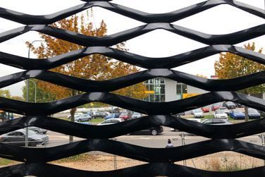 Eine Nahaufnahme eines schwarzen Maschendrahtzauns mit einem Parkplatz im Hintergrund.