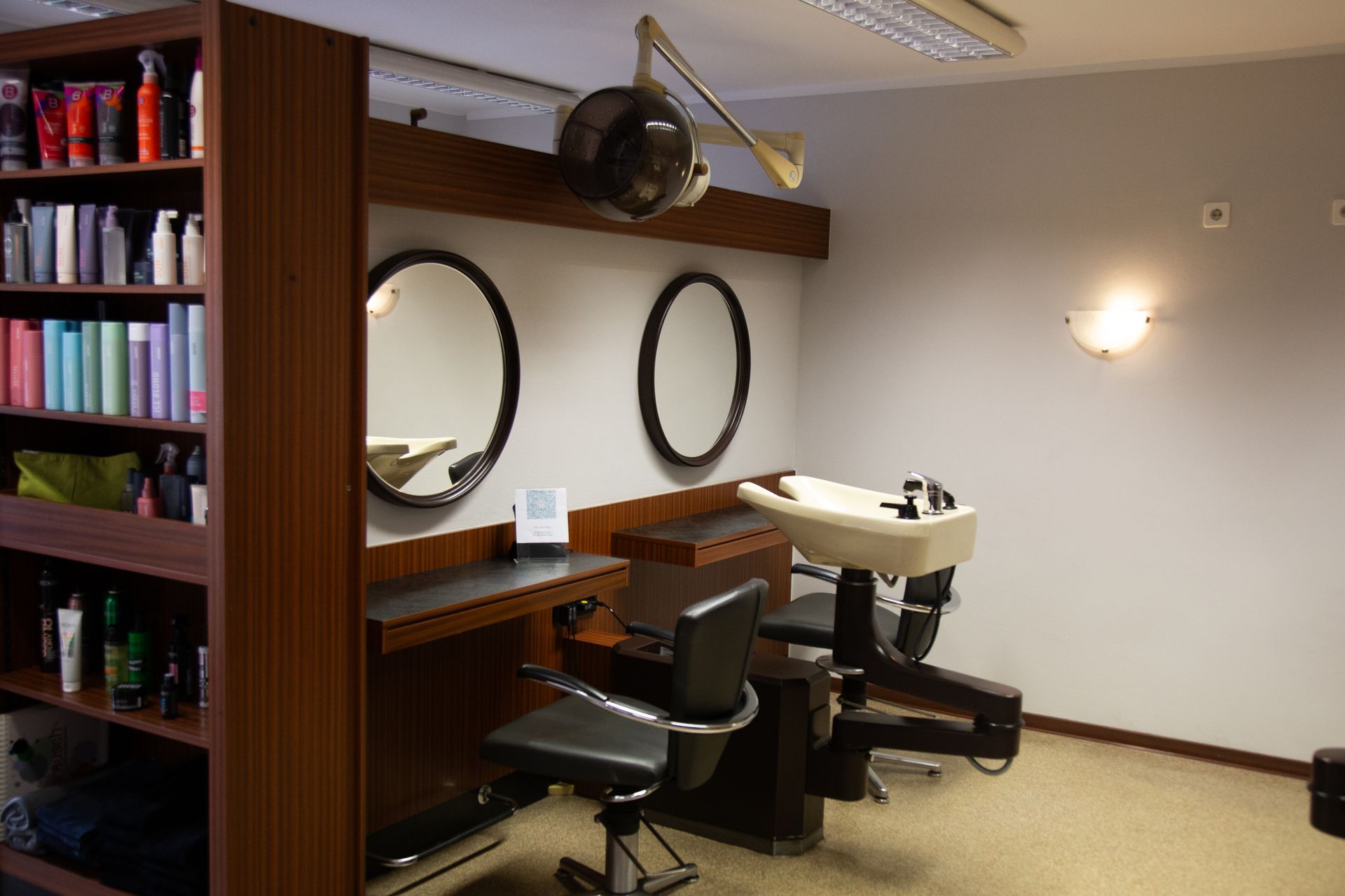 Interieur eines Friseursalons: Spiegel, Frisierplatz, Shampoo-Stuhl, Haarpflegeprodukte in Regalen.