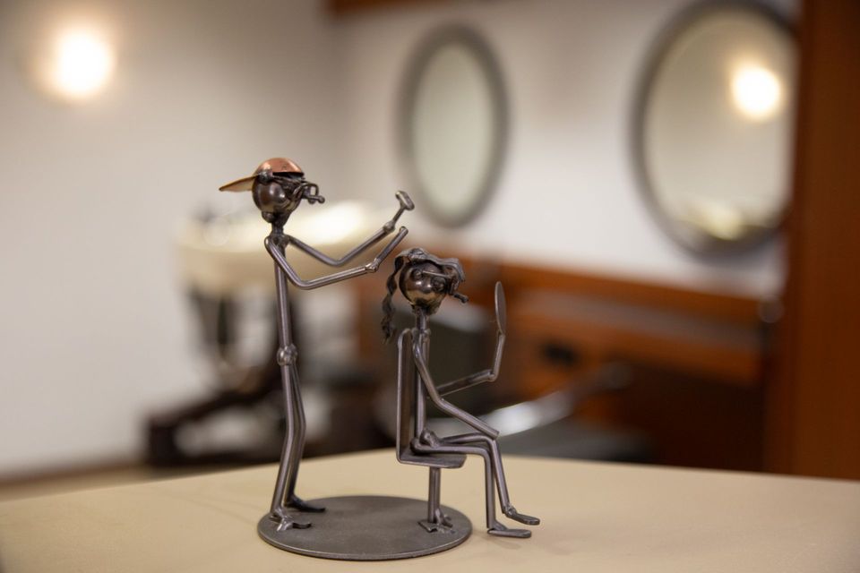 Metallskulptur eines Barbiers, der einem Kunden in einem Friseursalon die Haare schneidet.
