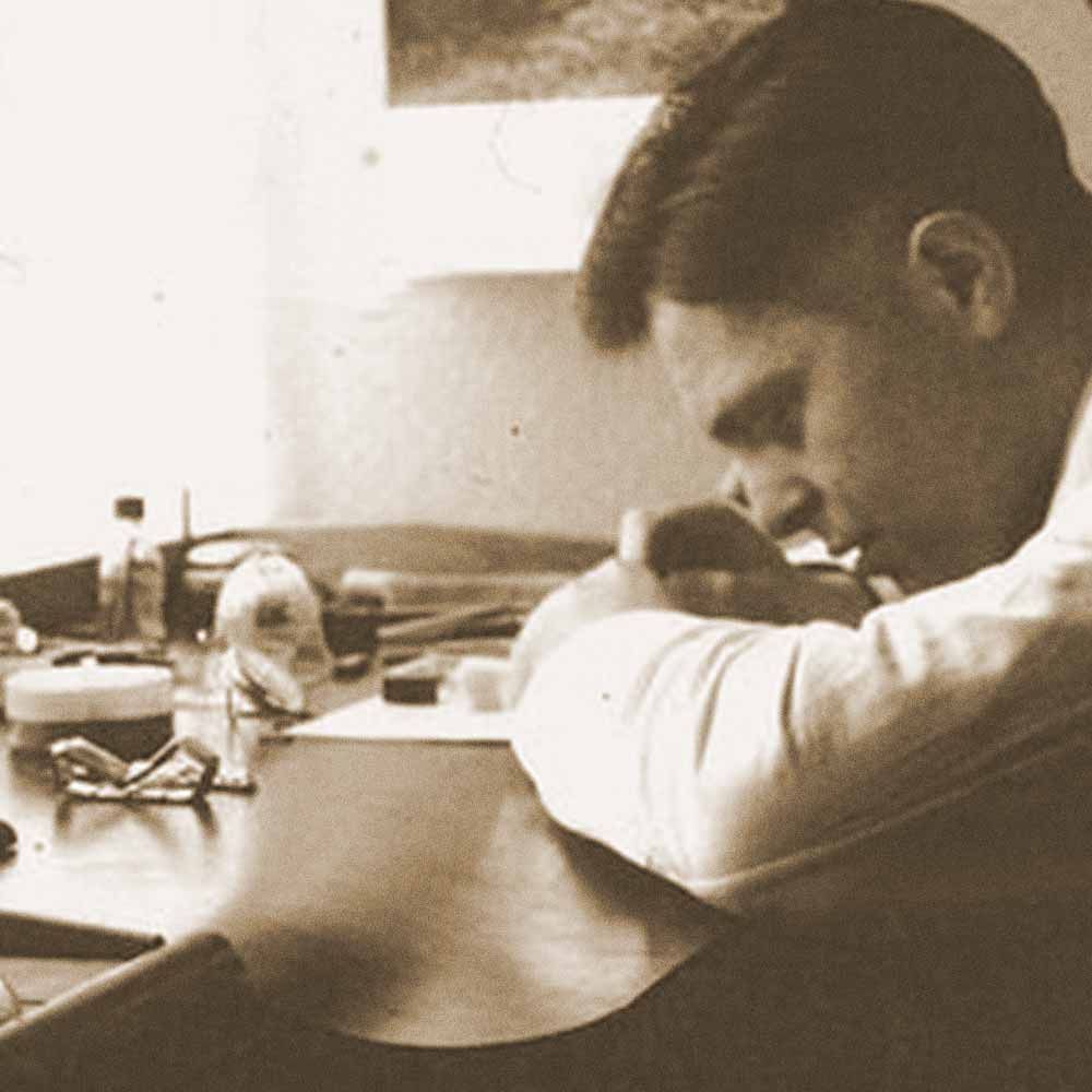 Ein Mann sitzt an einem Schreibtisch und schreibt auf ein Stück Papier