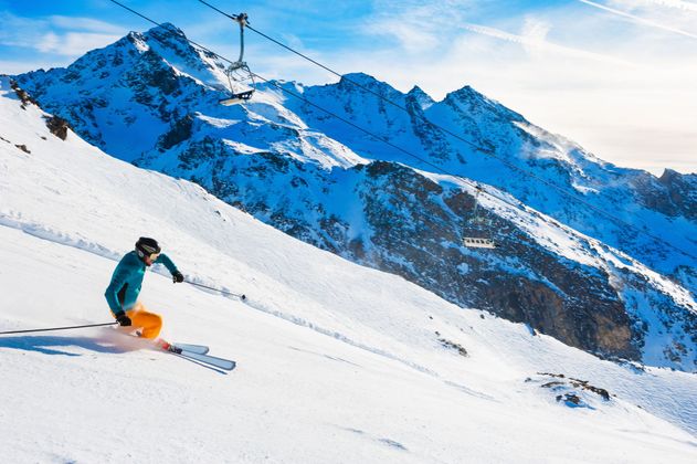 Skieur en veste turquoise dévalant une pente enneigée sous un ciel bleu.