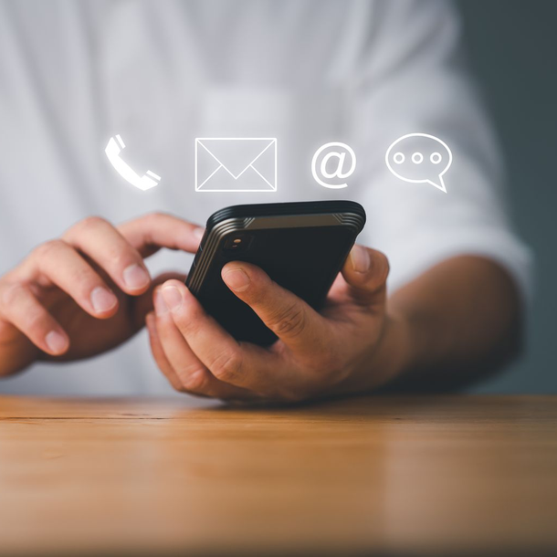 Des mains tenant un smartphone avec des icônes de messagerie flottant au-dessus.