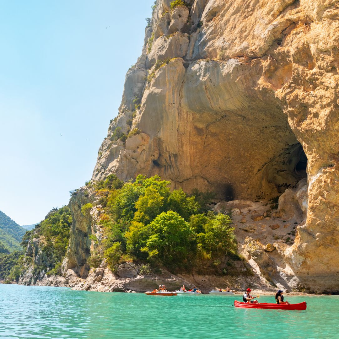 Des personnes font du kayak le long d'une imposante falaise côtière et d'un rivage verdoyant.