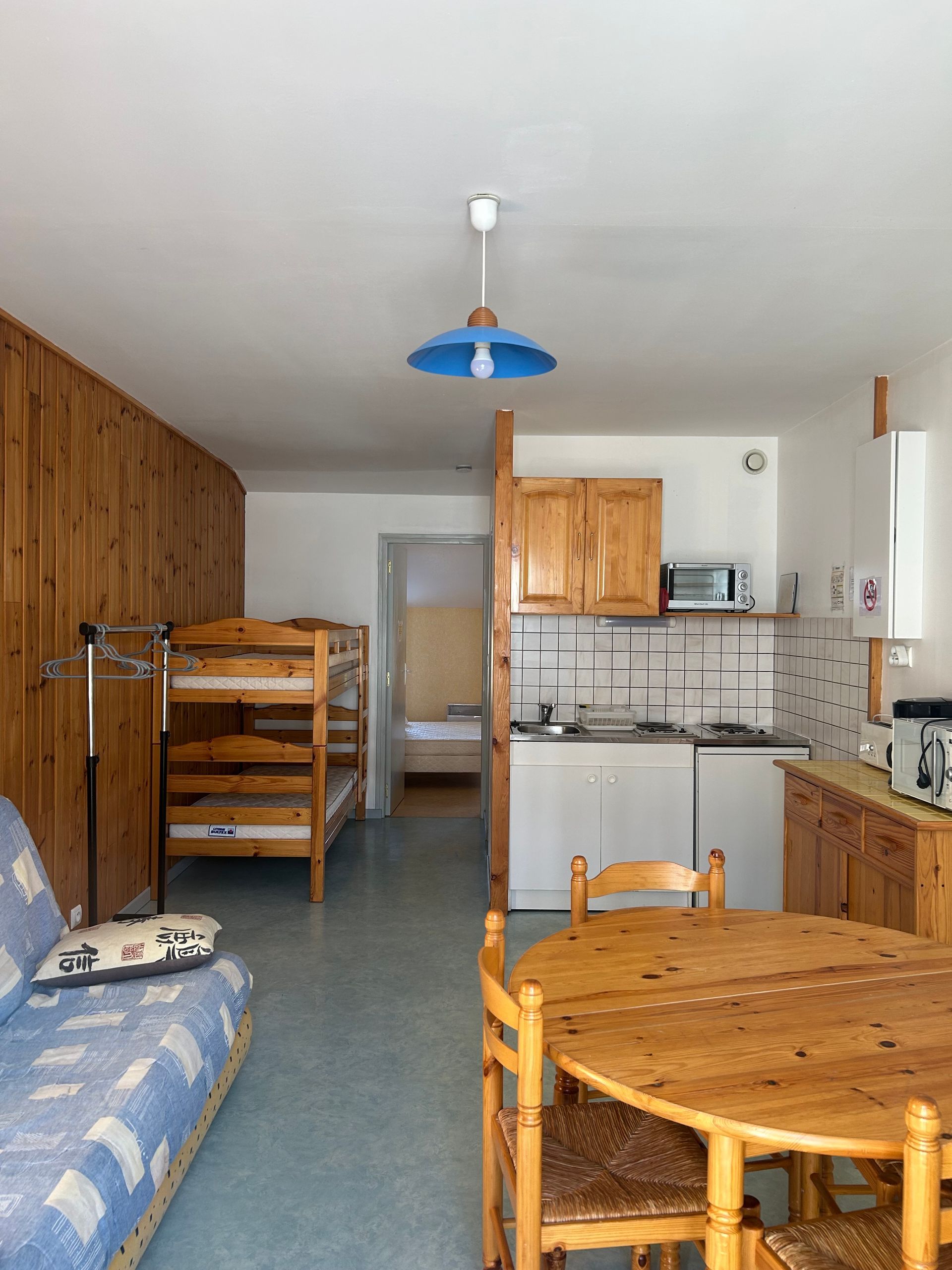 Petit coin cuisine-salle à manger avec meubles en bois, lit superposé et kitchenette carrelée.