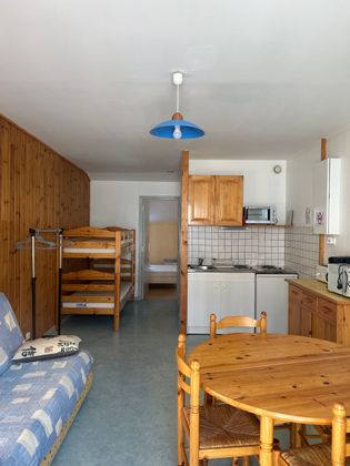 Petite cuisine de studio avec meubles en bois, lits superposés et plafonnier bleu.