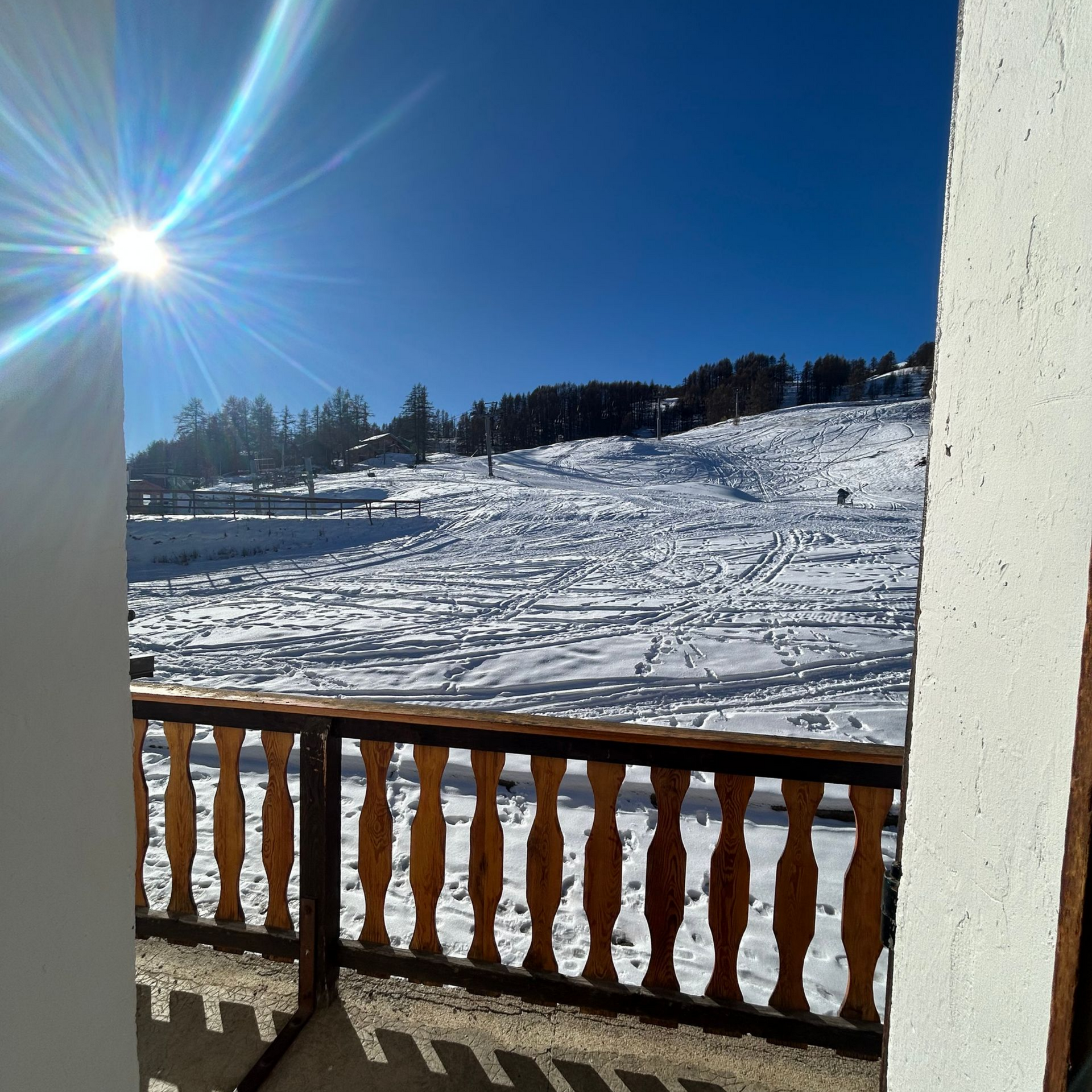 Colline enneigée sous un soleil éclatant, vue depuis un balcon.