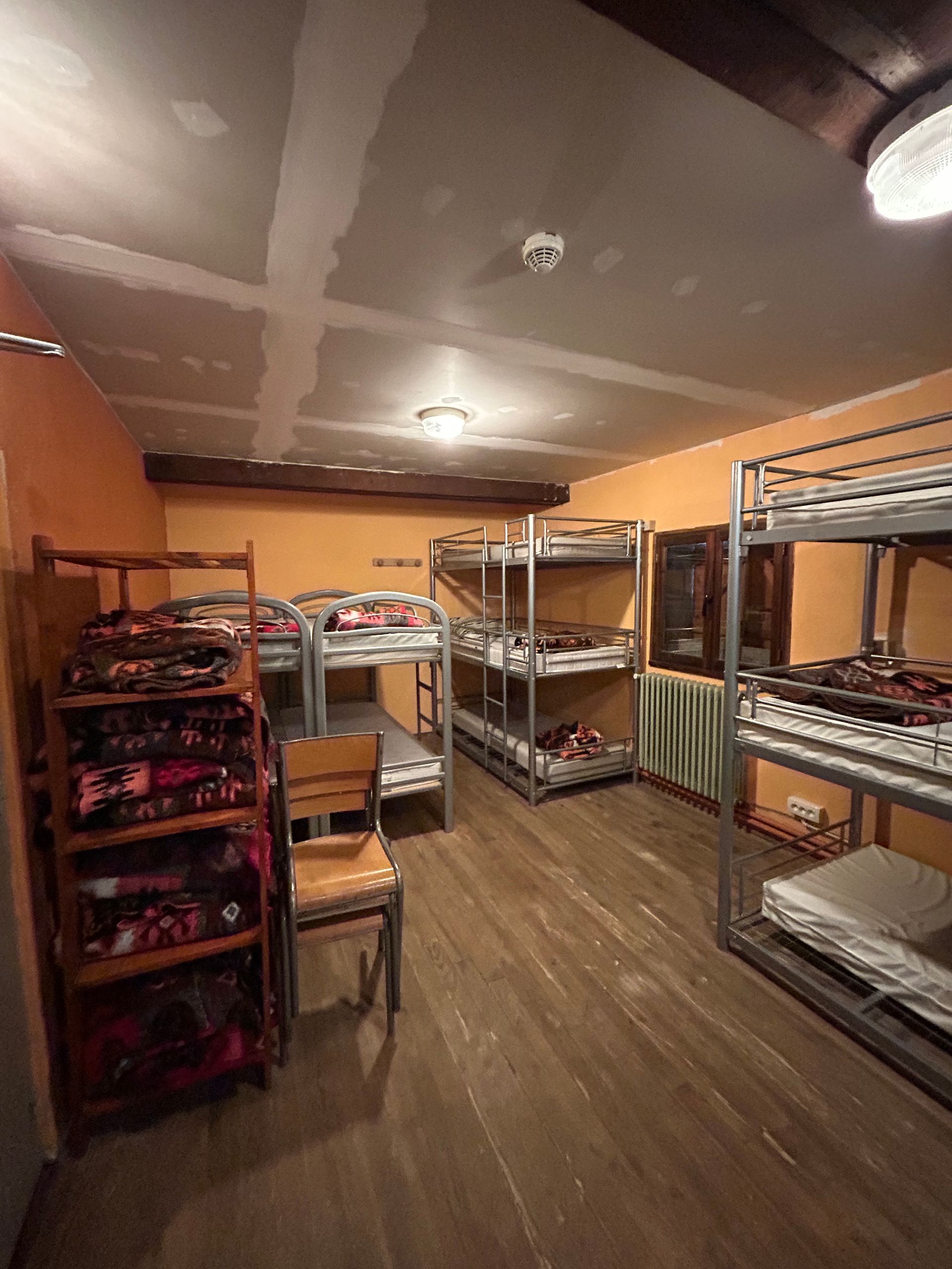 Chambre de dortoir avec lits superposés en métal, étagères et parquet.