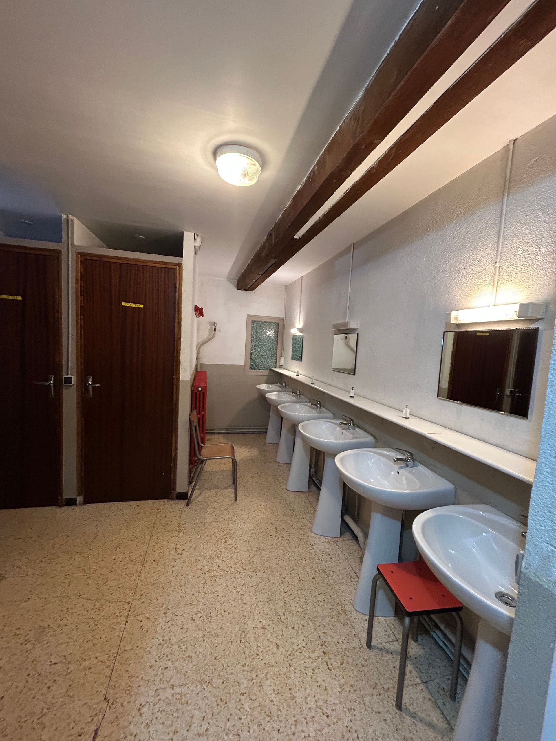 Toilettes étroites avec lavabos le long d'un mur, miroirs, tabourets et casiers.