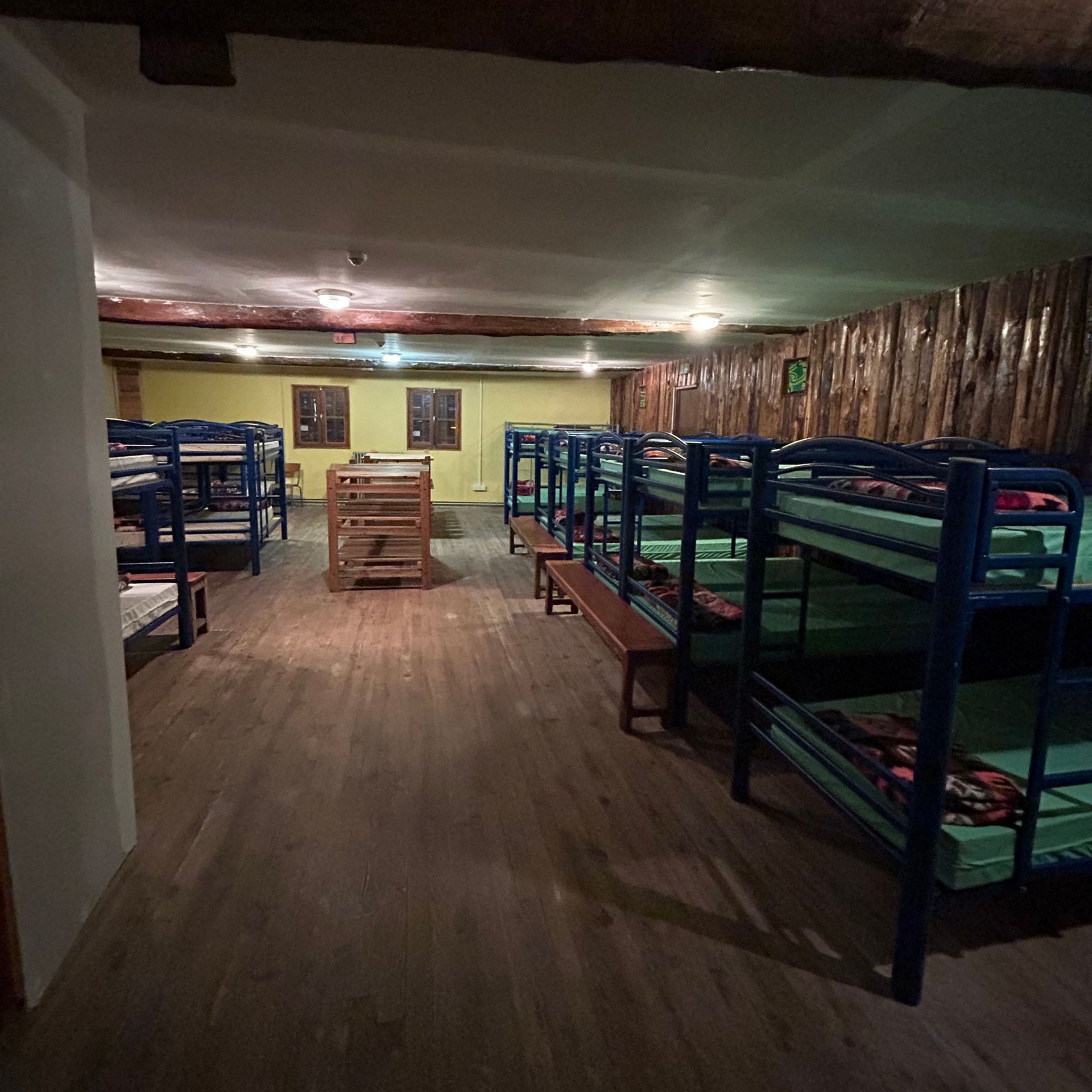Dortoir avec des rangées de lits superposés bleus et un plancher en bois.