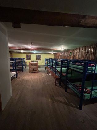 Chambre de dortoir avec rangées de lits superposés en métal, plancher en bois et éclairage tamisé.