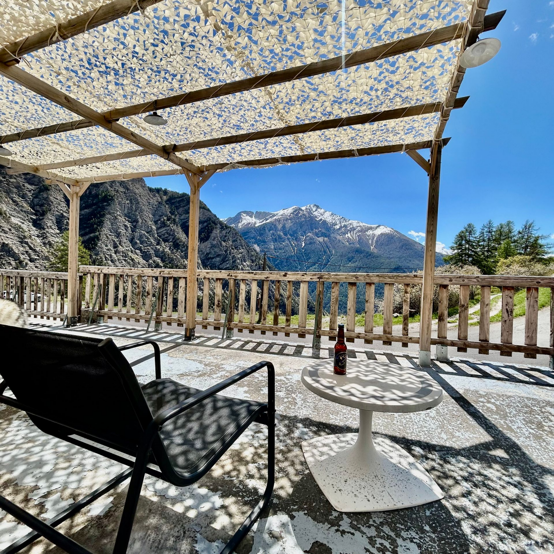 Terrasse avec chaise et table noires sous un auvent, donnant sur les montagnes enneigées.