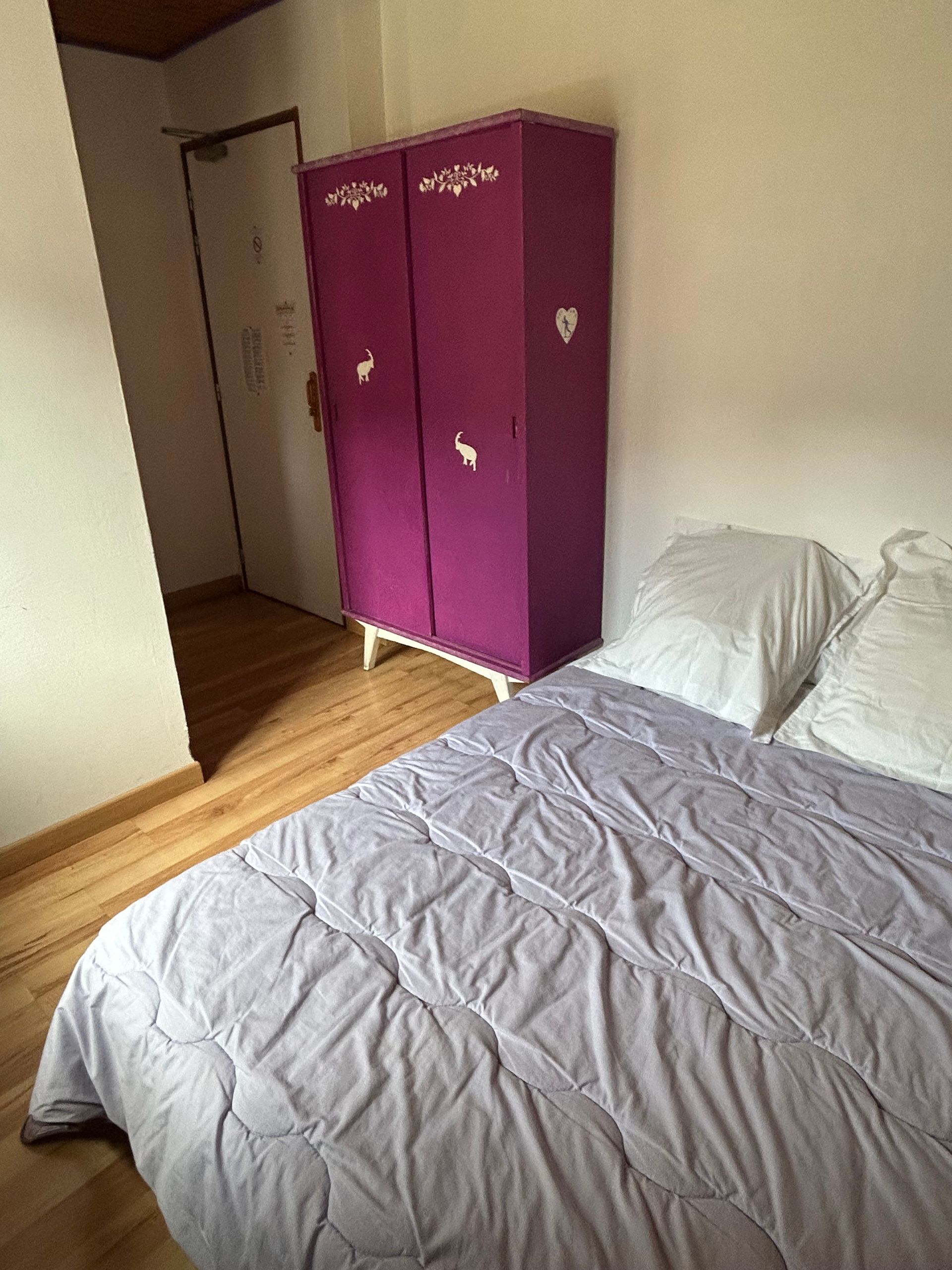 Petite chambre avec un lit au premier plan et une armoire violette contre le mur.
