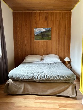 Petite chambre avec un lit adossé à un mur lambrissé, une photo de montagne au-dessus et une lampe sur la droite.