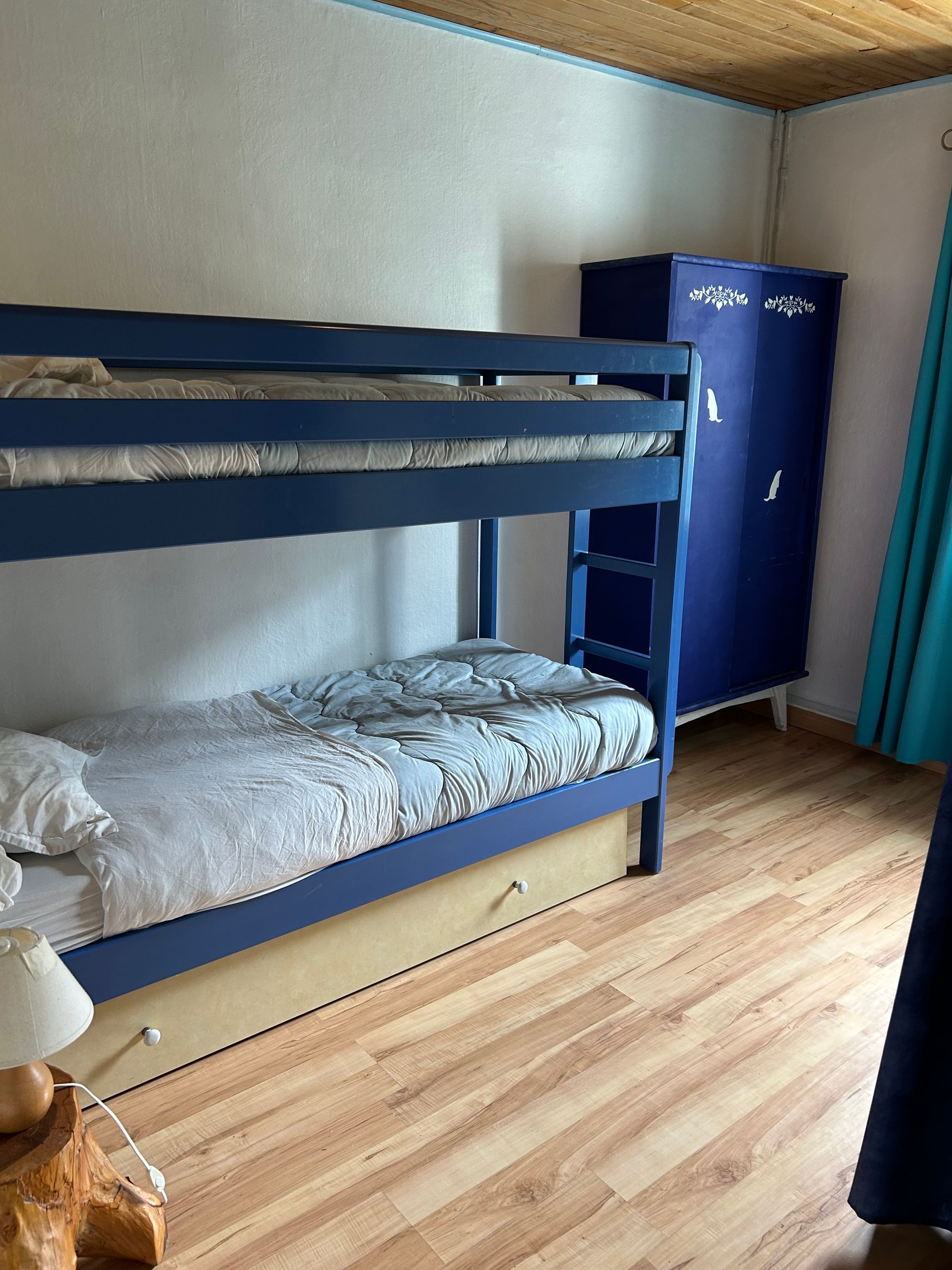 Lit superposé bleu dans une petite chambre avec parquet et armoire d'angle.