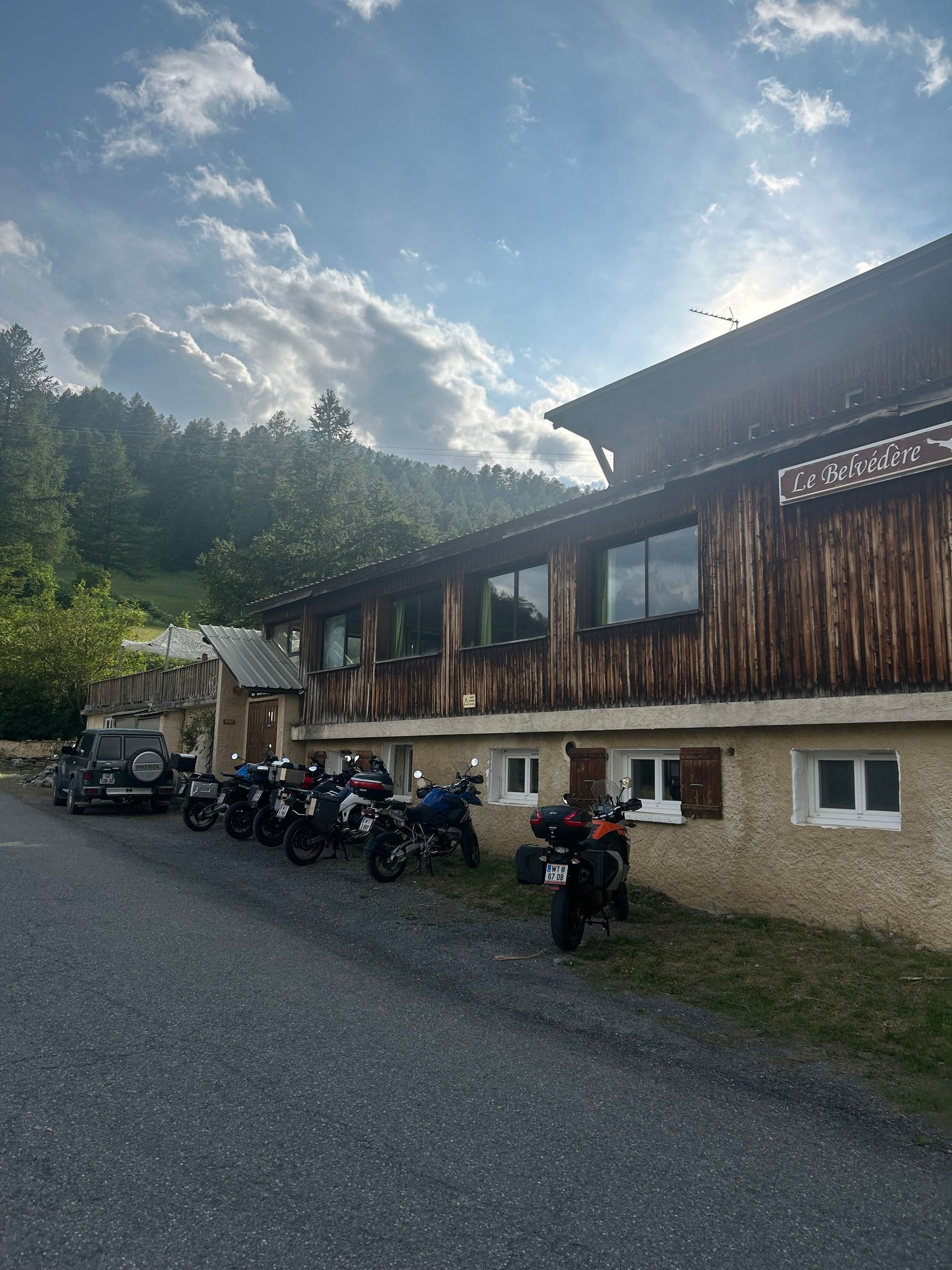 Extérieur rustique d'un chalet avec des motos garées au bord d'un chemin de gravier.