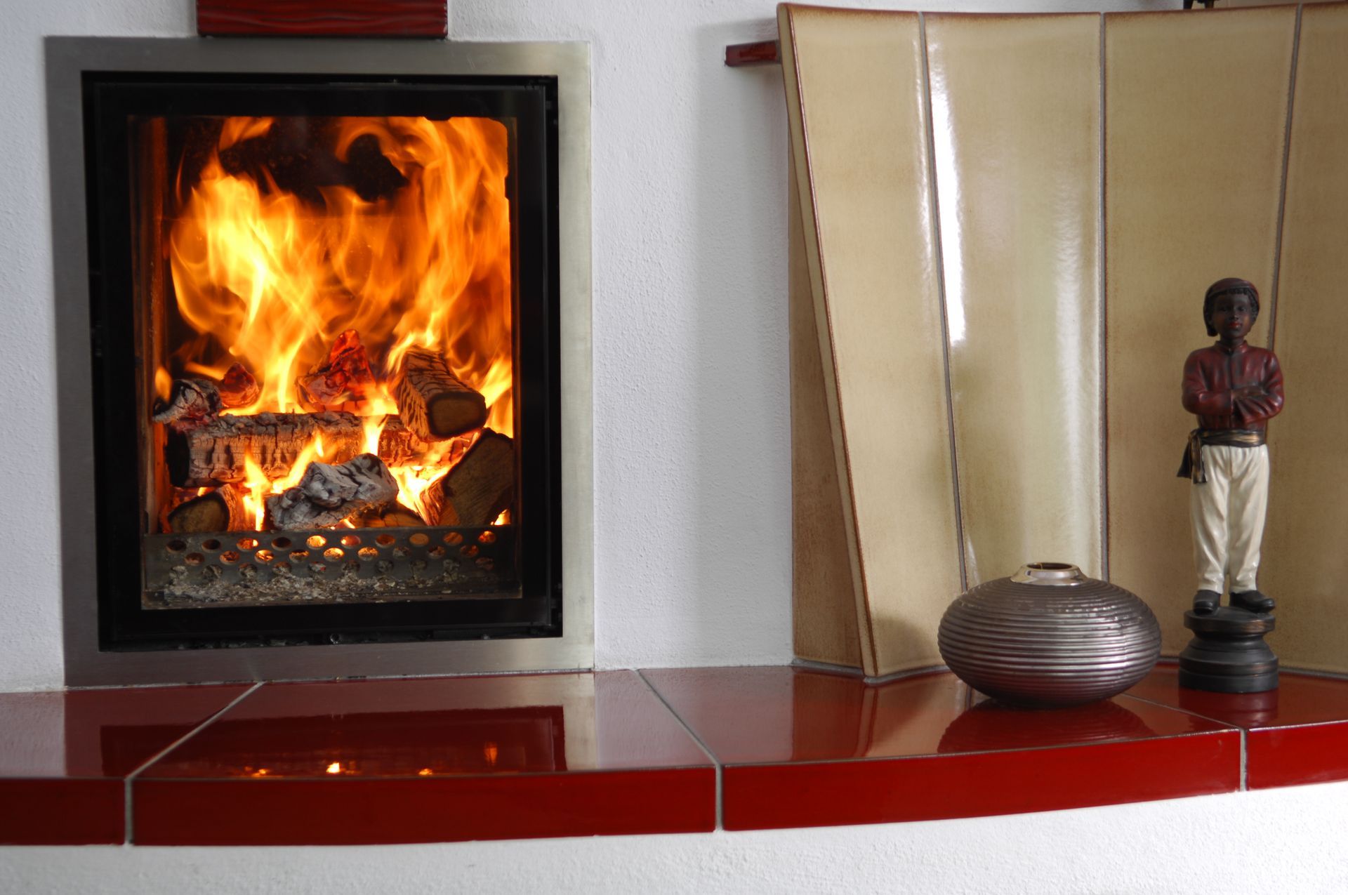 Ein brennender Kamin mit hellen Flammen neben einem dekorativen Regal mit Schale und einer Figur.