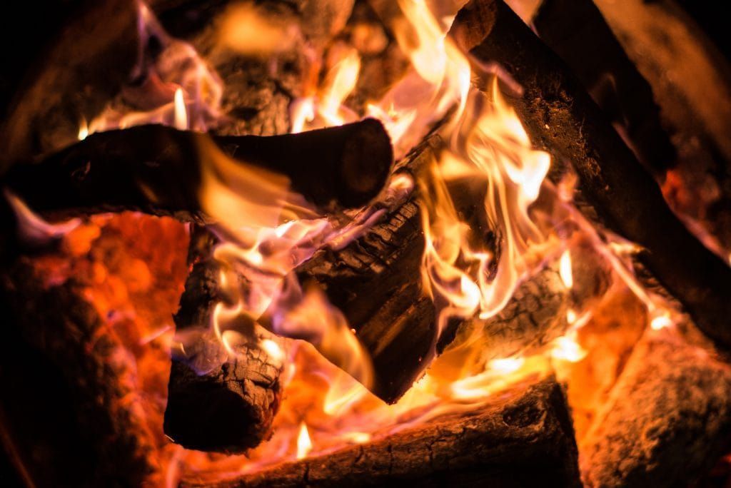 Brennende Holzscheite in einem Kamin mit hellorangefarbenen Flammen und glühenden Glutstücken.